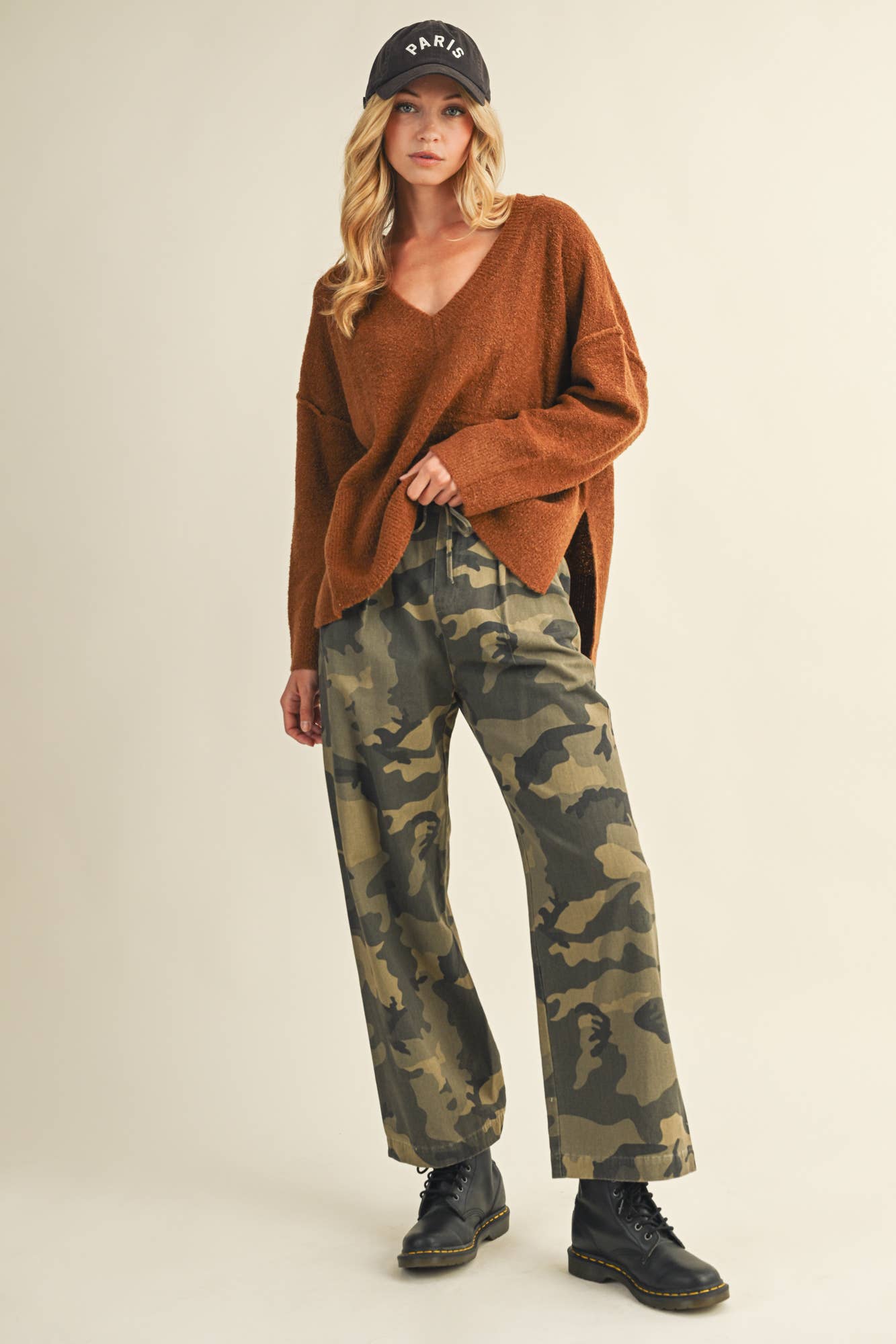 Woman in sweater, camo pants, and cap.